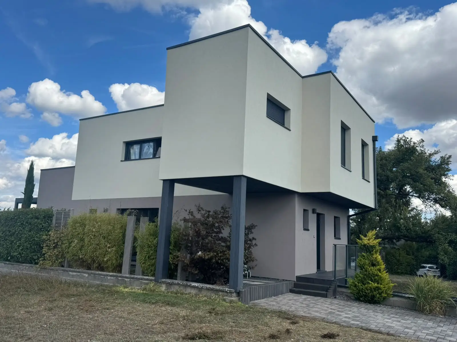 Maison contemporaine à toit plat, façades en enduit clair et gris, vue latérale