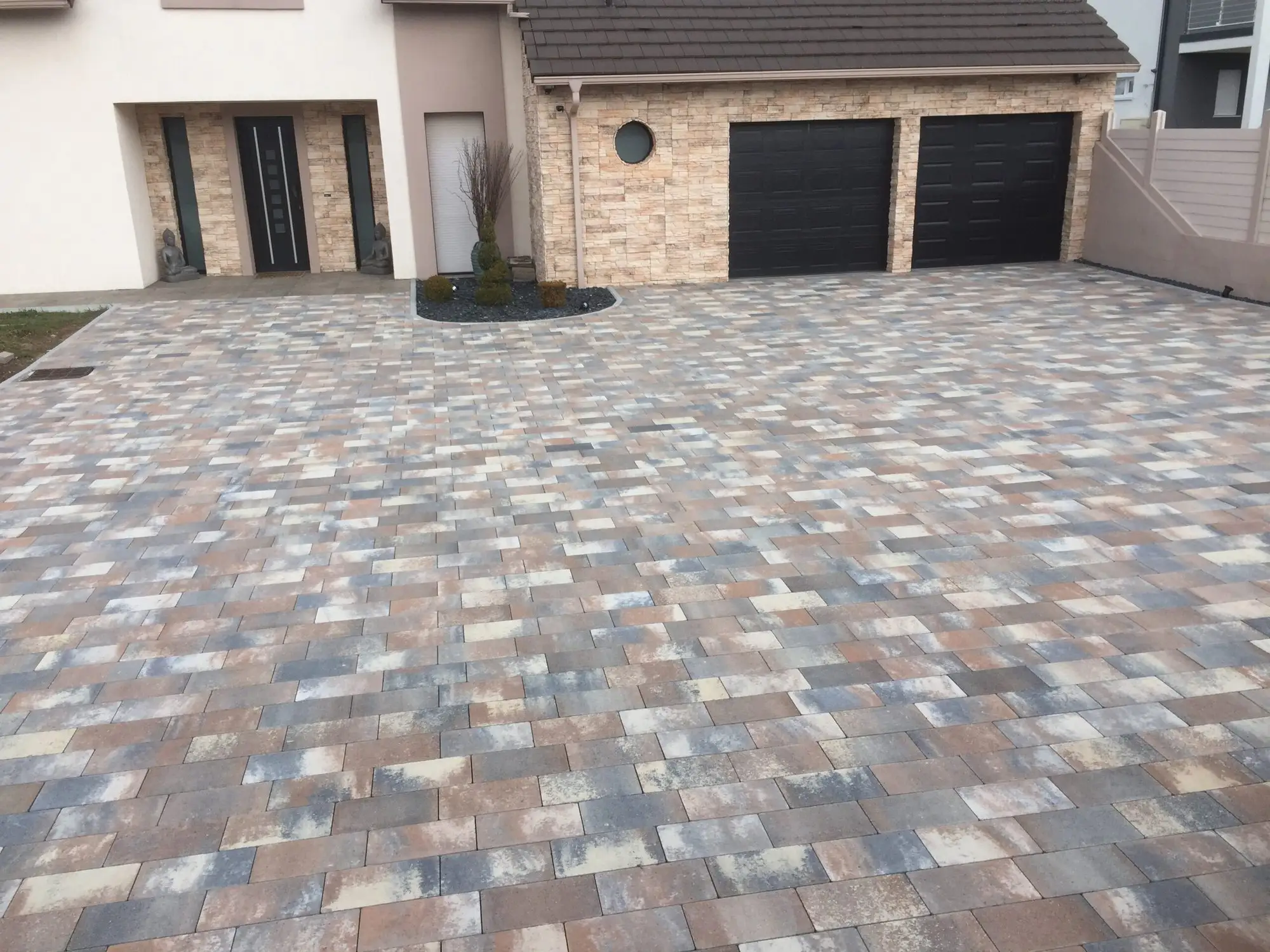 Cour et allée en pavés béton nuancés devant une maison neuve à double garage