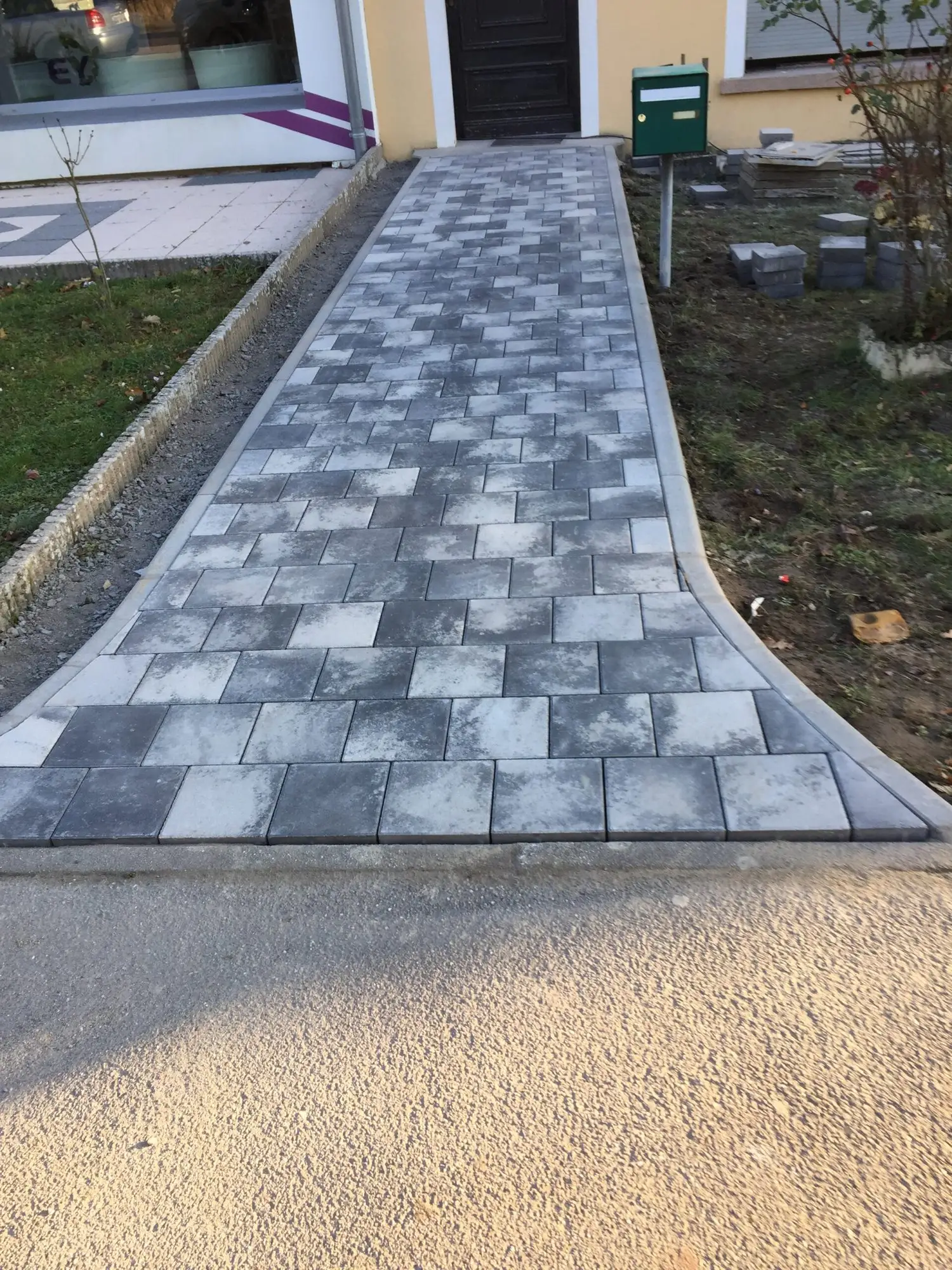 Allée en pavés gris traversant une pelouse, bordée de bordures béton
