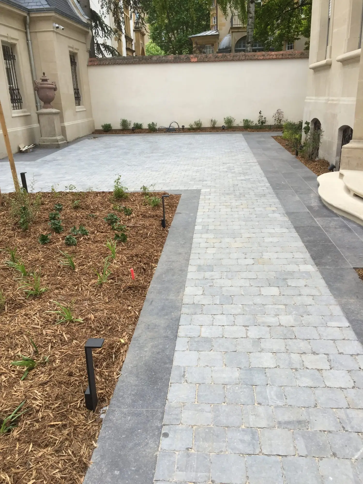 Cour pavée claire avec massifs plantés et bordures en pierre