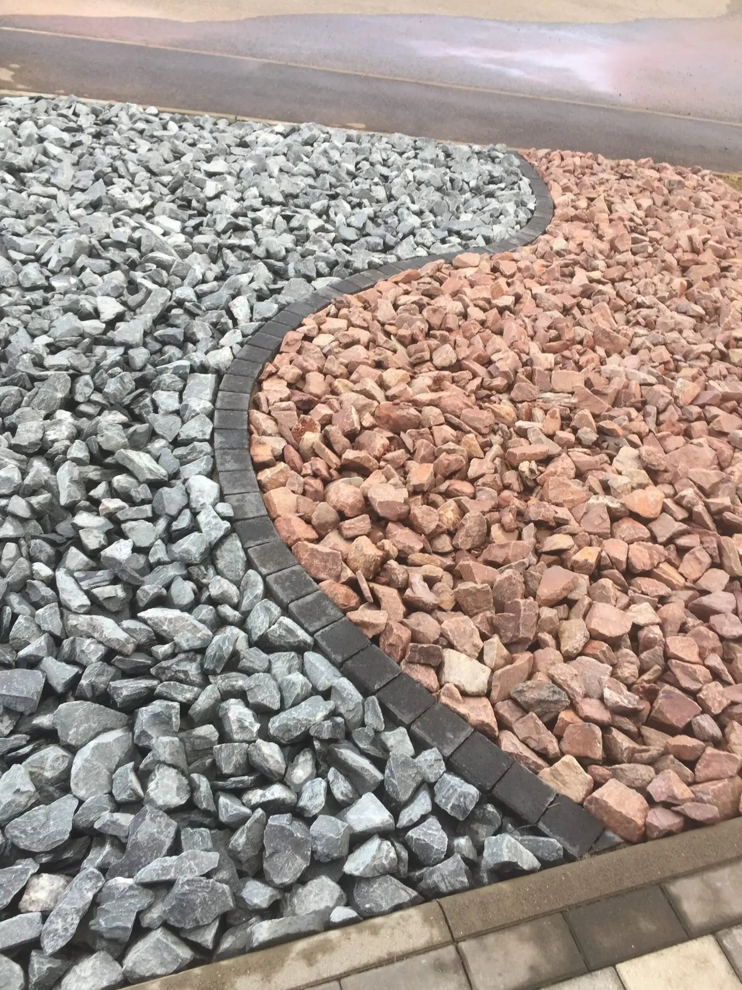 Massif décoratif en graviers gris et rouges séparés par une bordure courbe en pavés